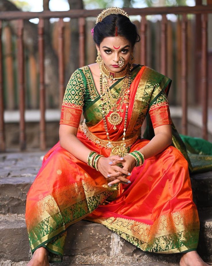 a woman in an orange and green sari sits on steps with her hands clasped