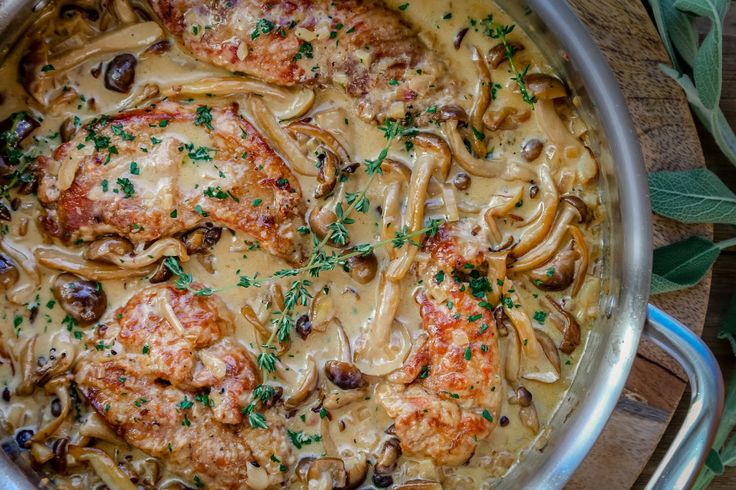 a pan filled with meat and mushrooms covered in gravy on top of a wooden table