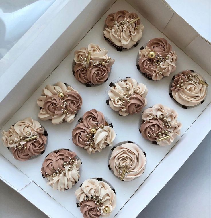 twelve cupcakes in a white box decorated with pink and brown frosting flowers