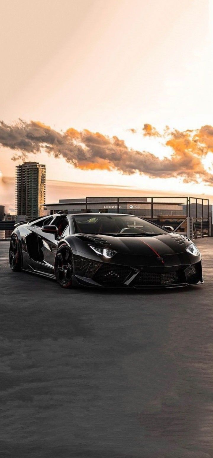 a black sports car parked in front of a parking lot at sunset with the sun behind it