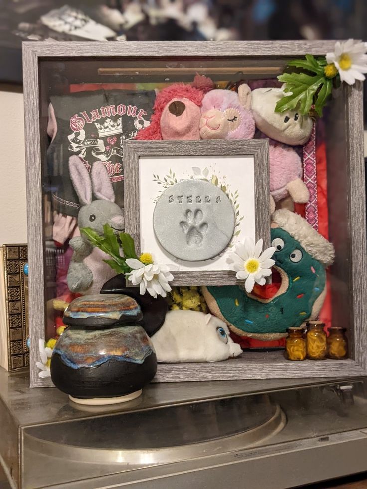 there are many stuffed animals in the shadow box on top of a table with flowers