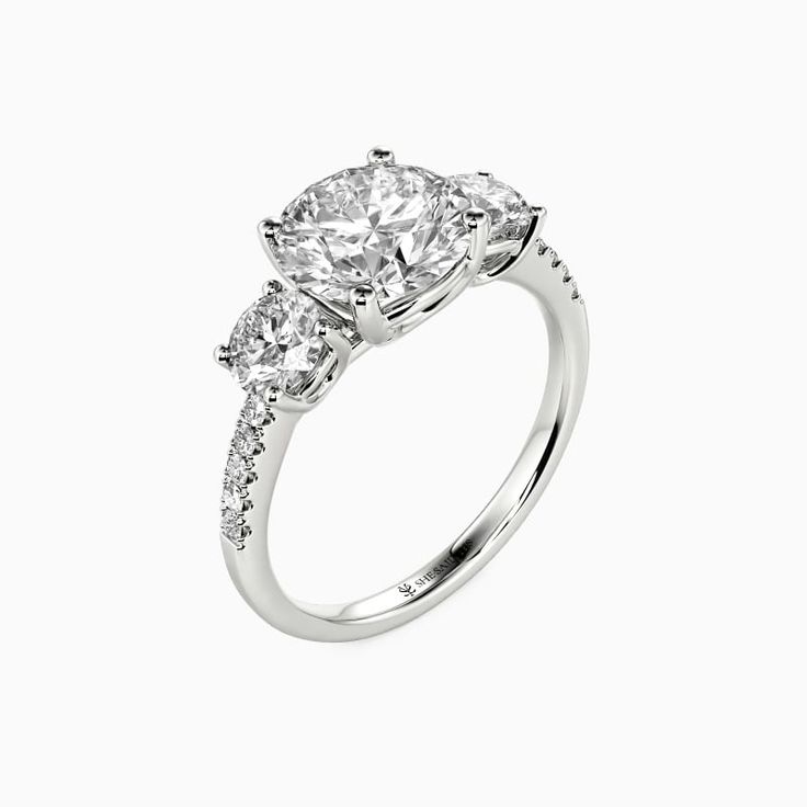 a three stone engagement ring with diamonds on the sides and an oval shaped diamond in the center