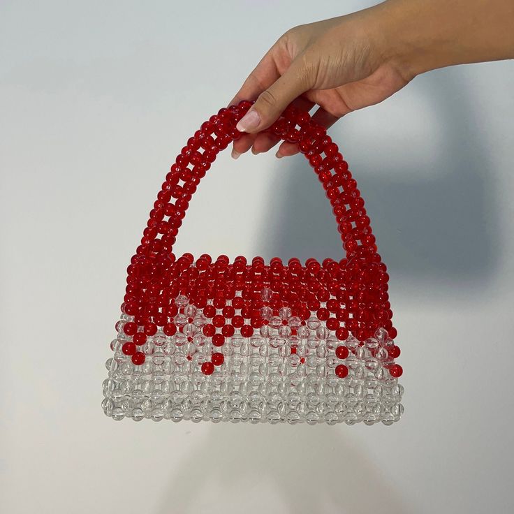 a hand holding a red and white beaded purse