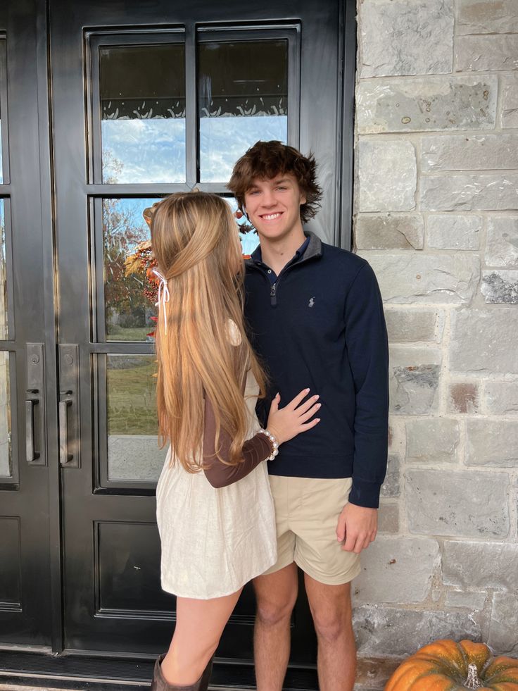 a young man and woman standing in front of a door with their arms around each other