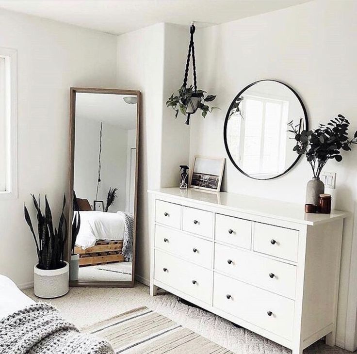 a bedroom with white furniture and plants on the dresser next to a large round mirror