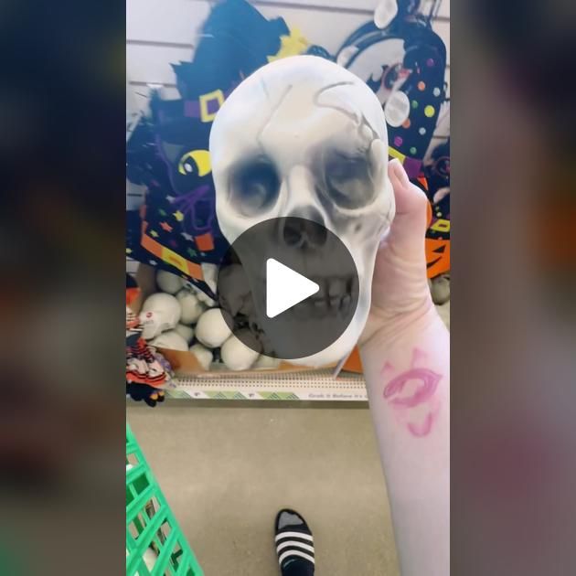 a person holding up a fake skull in front of a store display with other items