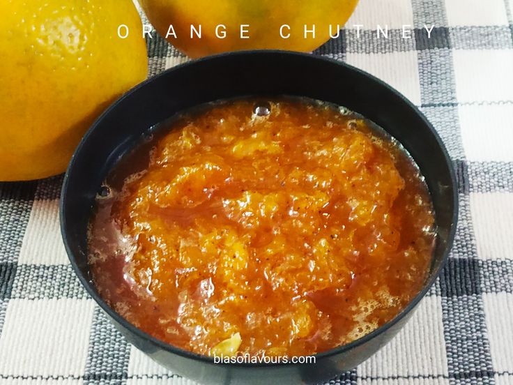 an orange chut in a black bowl next to two lemons on a checkered table cloth