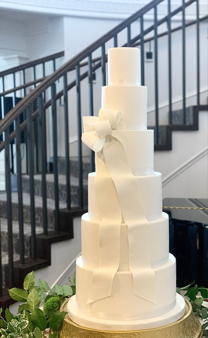 a white wedding cake sitting on top of a table next to a stair case with greenery