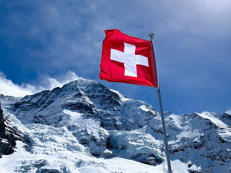 a swiss flag flying in front of a snowy mountain