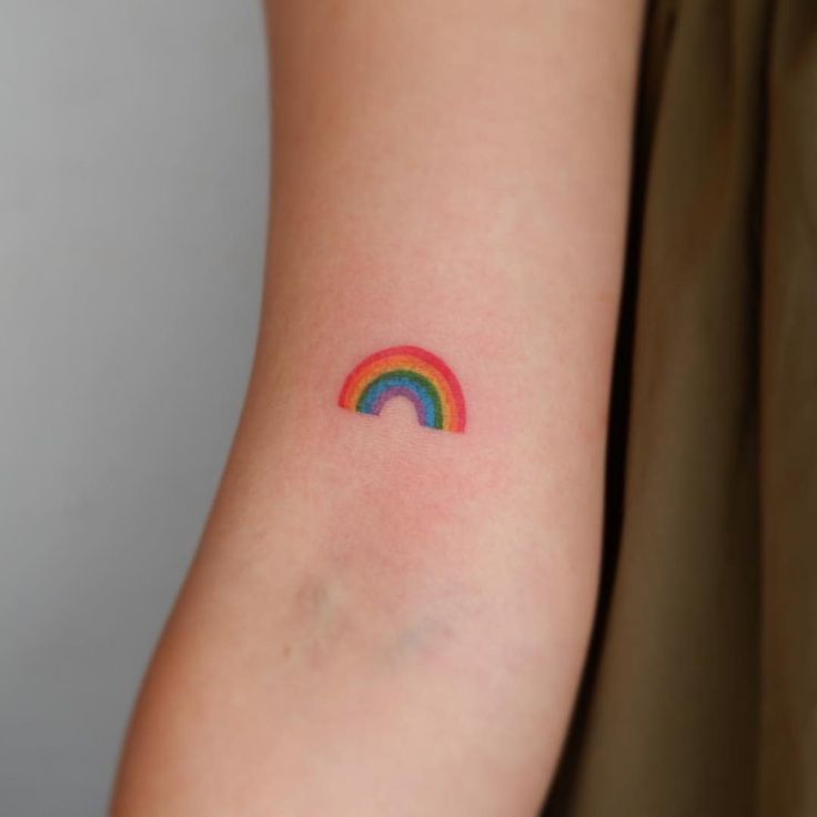 a woman's arm with a small rainbow tattoo on the left side of her arm