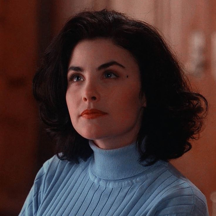 a woman with dark hair wearing a blue turtle neck sweater looking off to the side