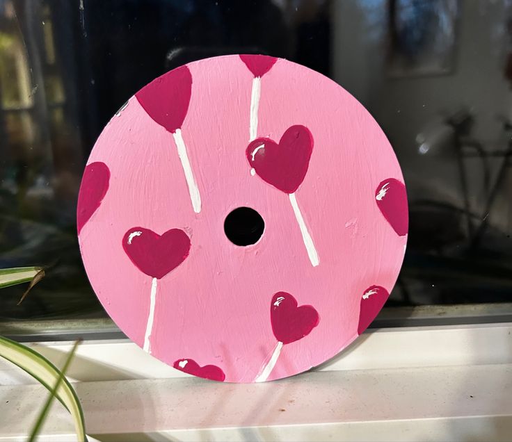 a pink and white round object with hearts on it sitting on a window sill