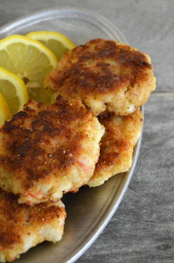 three crab cakes on a plate with lemon wedges