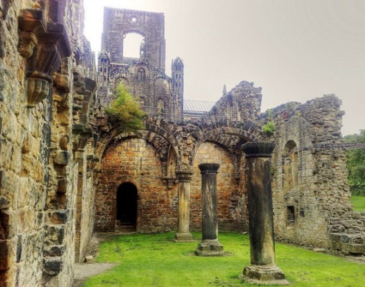 the ruins of an old castle with green grass and stone pillars in front of it