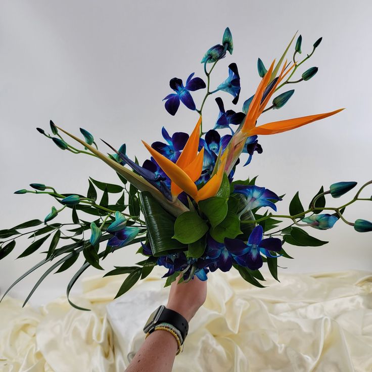 a bouquet of blue and orange flowers in someone's hand on a white sheet