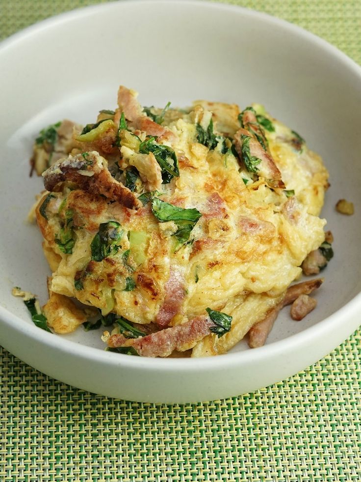 an omelet with bacon and spinach in a white bowl on a green tablecloth