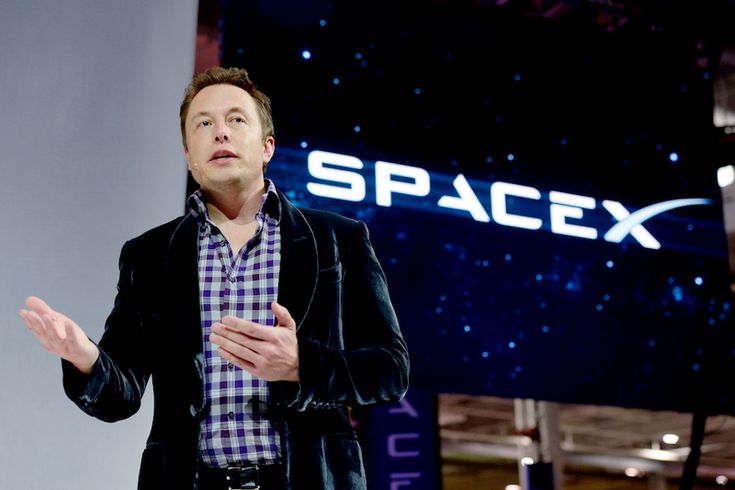 a man standing in front of a spacex sign with his hands out to the side