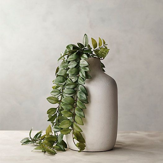 a white vase filled with green leaves on top of a table