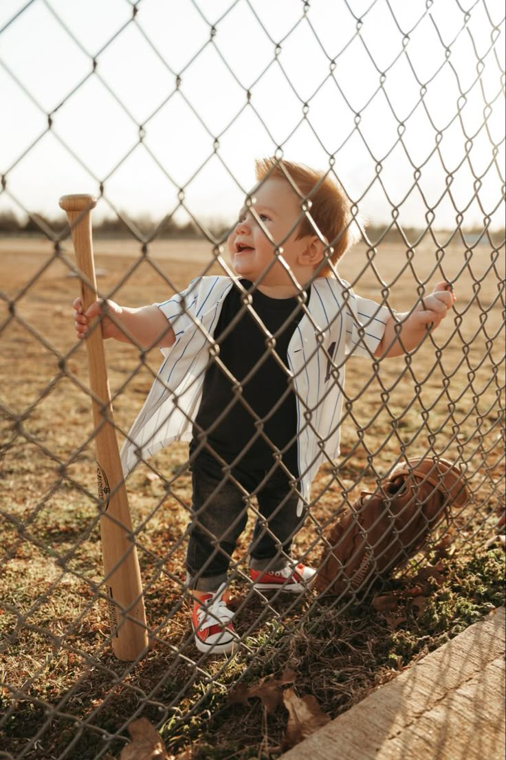 a young boy holding a baseball bat behind a fence