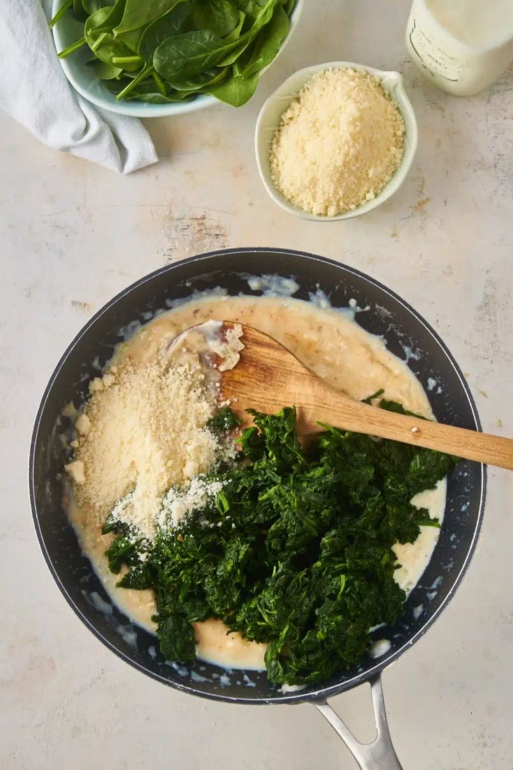 spinach and other ingredients in a skillet on a white counter top with a wooden spoon