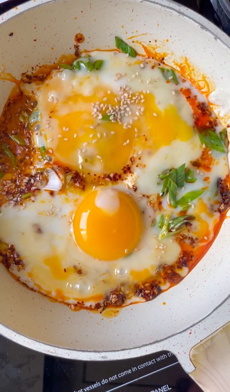 two fried eggs in a skillet on top of a stove burner with seasoning