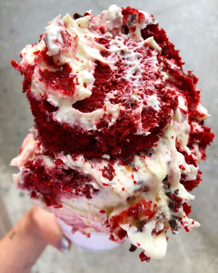 someone holding up a red velvet cake with white frosting