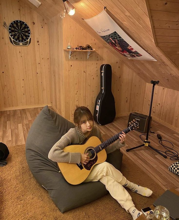 a person sitting on a bean bag chair playing an acoustic guitar in a room with wood paneling