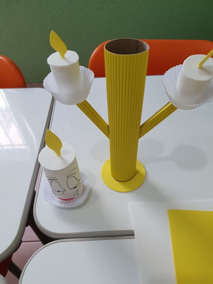 a yellow vase sitting on top of a white table next to two cups with lids