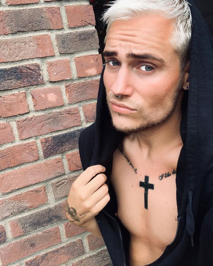 a man with white hair wearing a black hoodie and cross tattoo on his chest