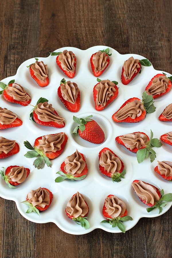 chocolate cheesecake deviled strawberries are arranged on a white platter with green leaves