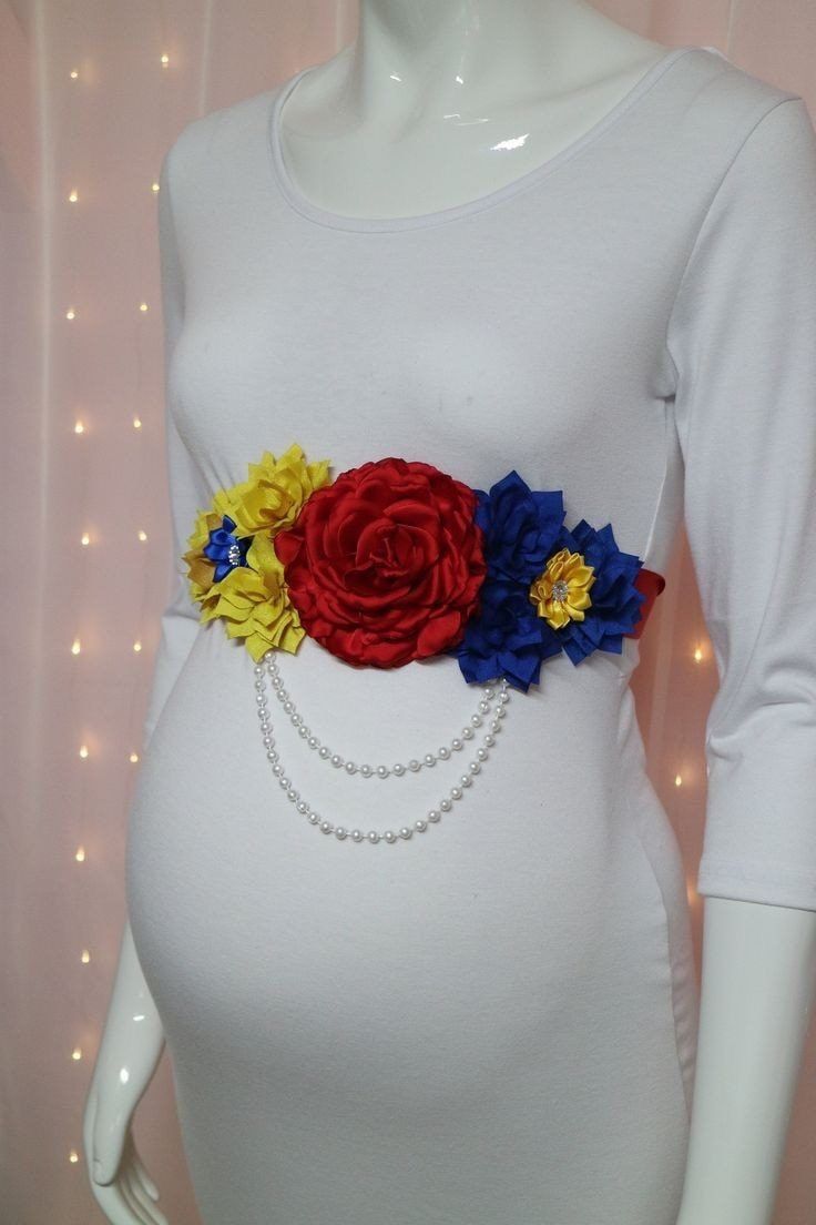 a pregnant woman wearing a white shirt with flowers on it's belt and pearls around the waist