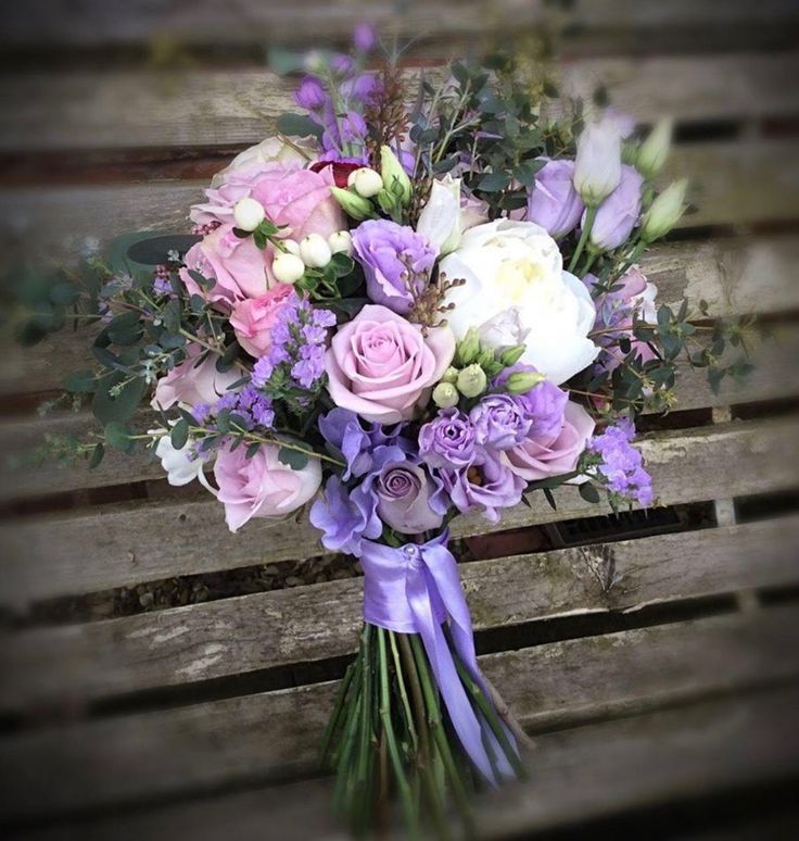 a bridal bouquet sitting on top of a wooden bench with purple and white flowers