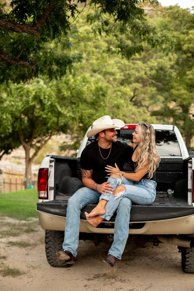 a man and woman sitting in the back of a pickup truck with their arms around each other