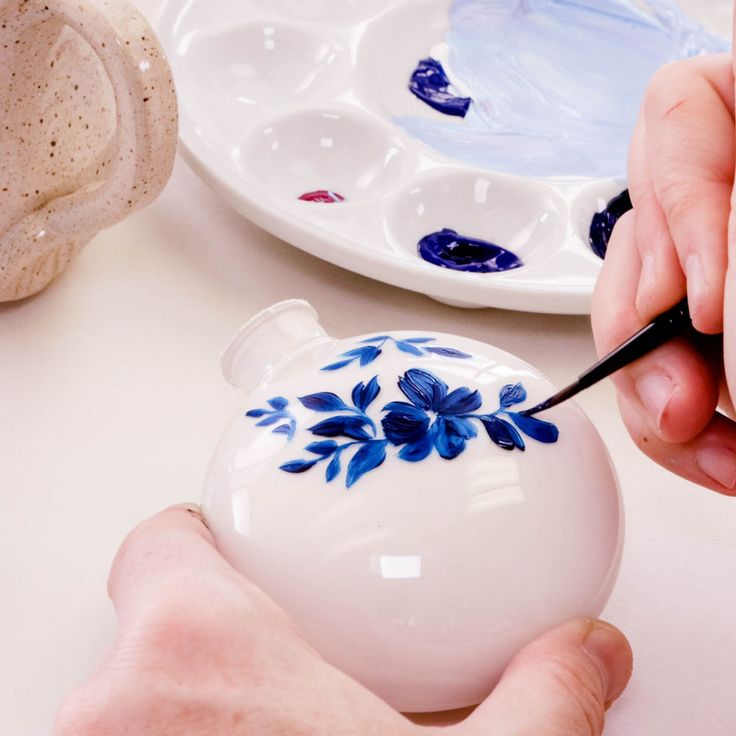 a person is decorating a small white ornament with blue flowers on it