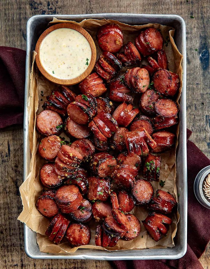 a tray filled with cooked sausages next to a bowl of sauce on top of a wooden table