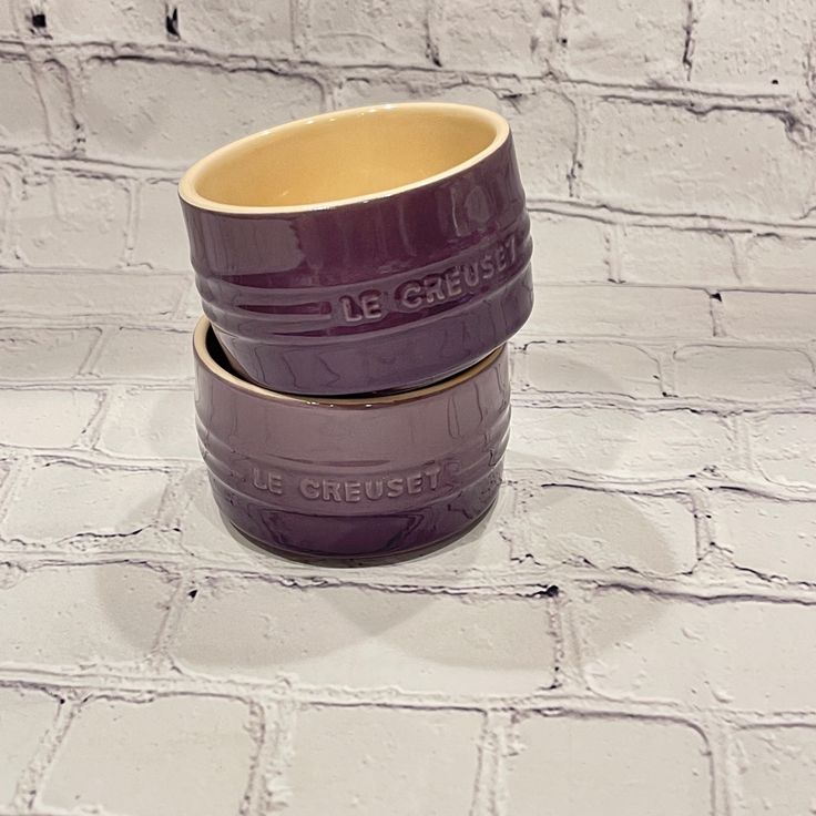 two purple cups sitting on top of each other in front of a white brick wall