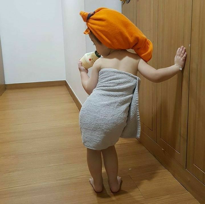 a small child wearing a towel and holding a toothbrush in his hand while standing on the floor