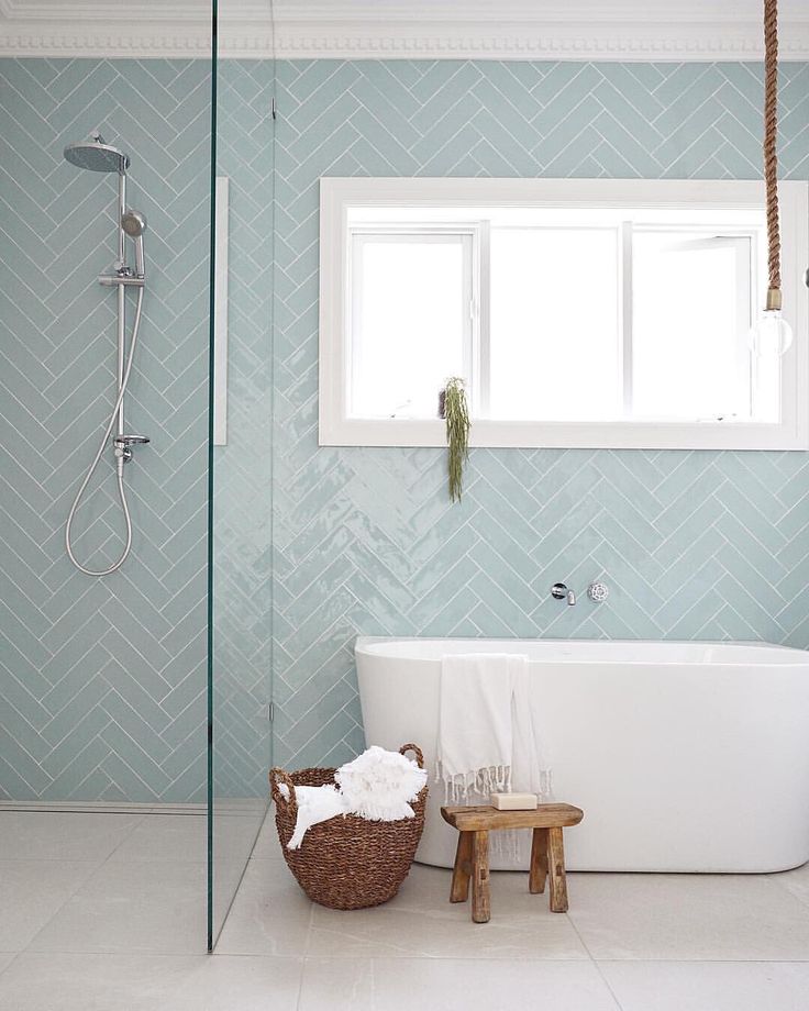 a white bath tub sitting under a window next to a wooden stool in a bathroom