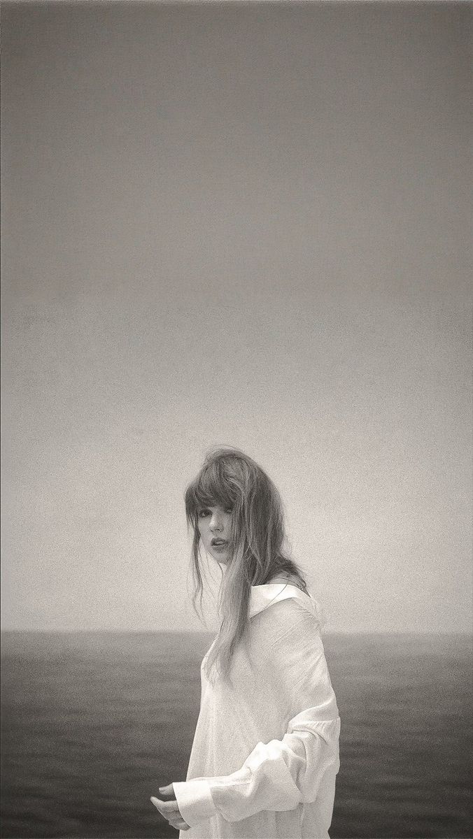 a black and white photo of a woman with long hair standing in front of the ocean