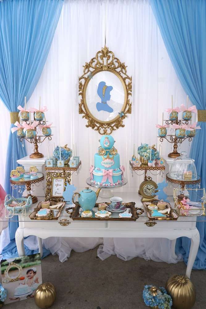 a table topped with lots of cakes and desserts next to a blue drapes