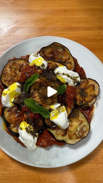 a white plate topped with eggplant and other food items on top of a wooden table