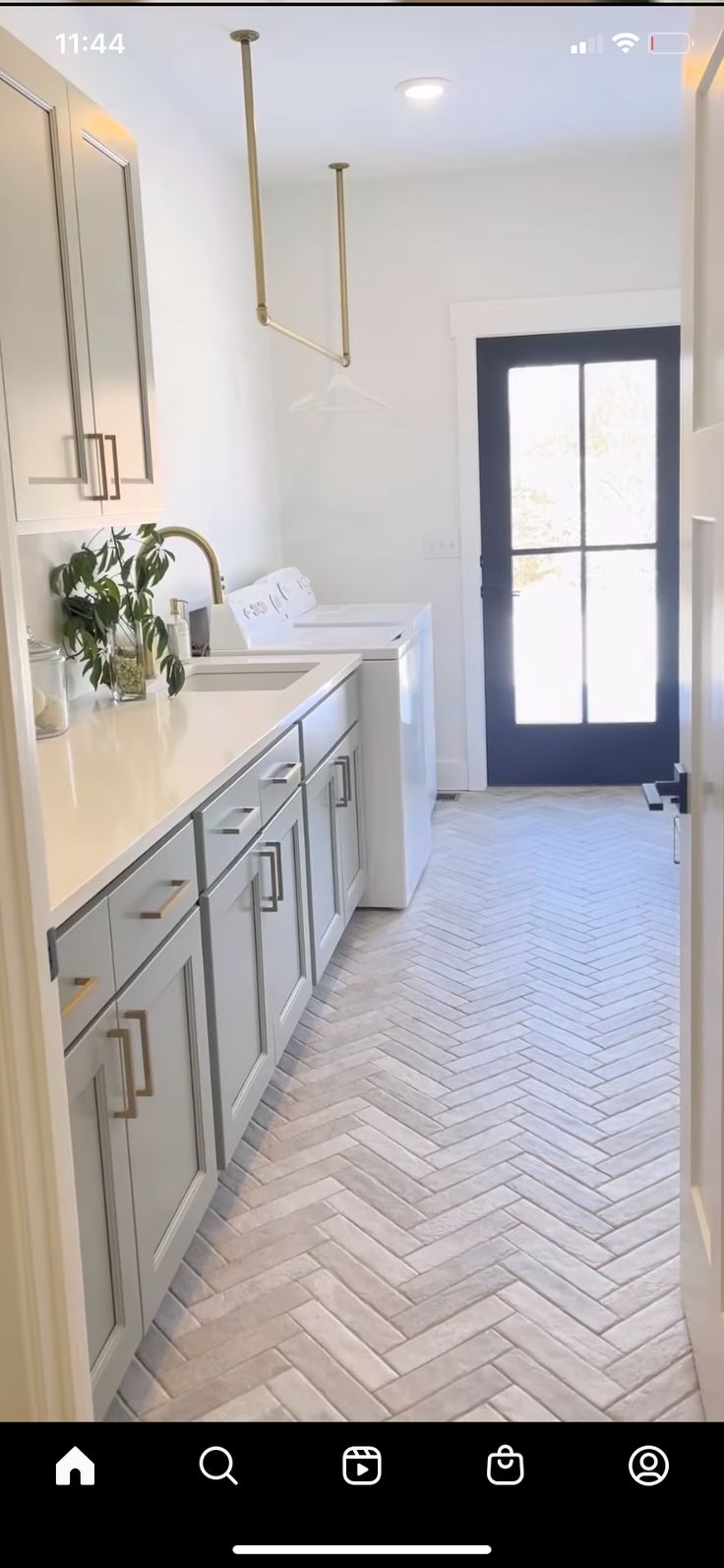 an empty kitchen with white cabinets and gray flooring is seen from the hallway leading to the front door