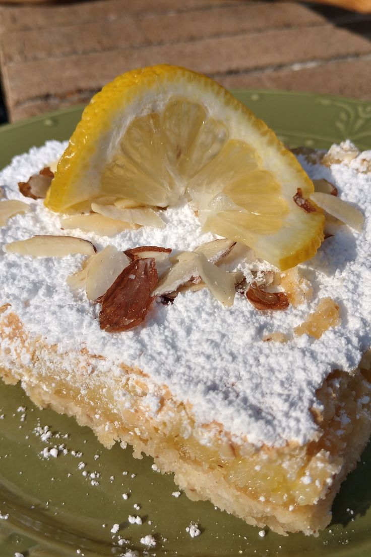 a slice of lemon cake with powdered sugar and fruit toppings on a green plate