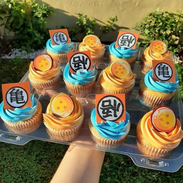 cupcakes with yellow frosting and blue icing on a tray in front of some bushes