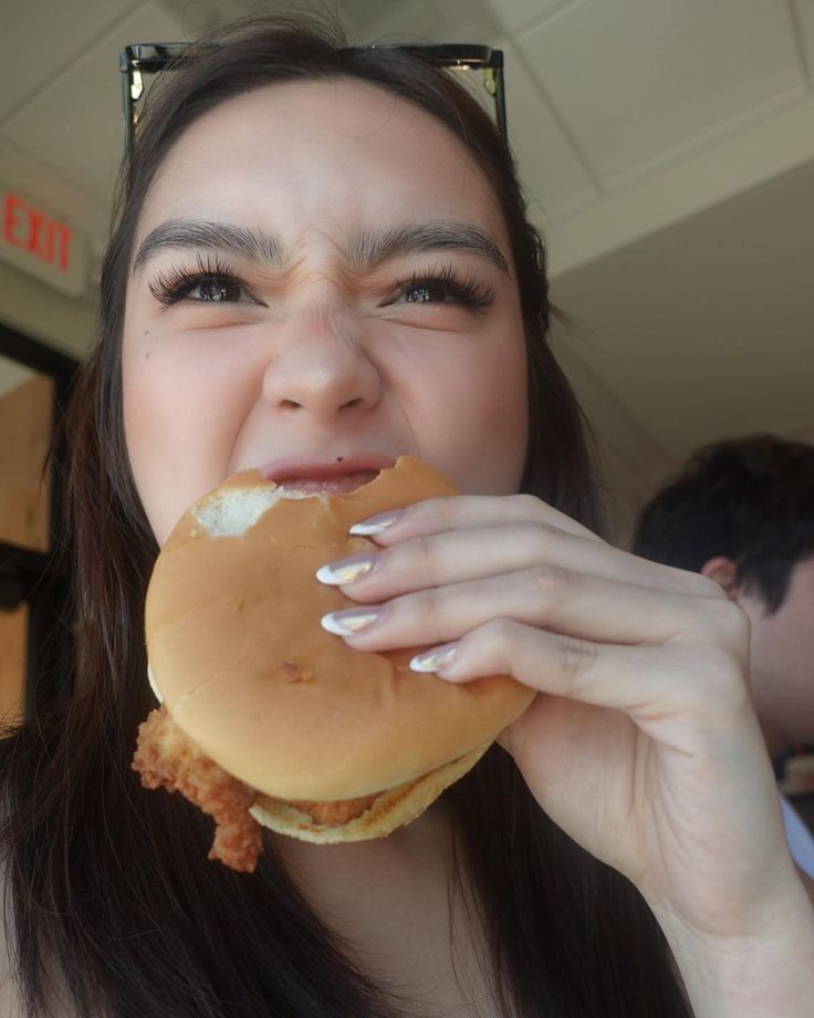 a woman eating a large hamburger in front of her face