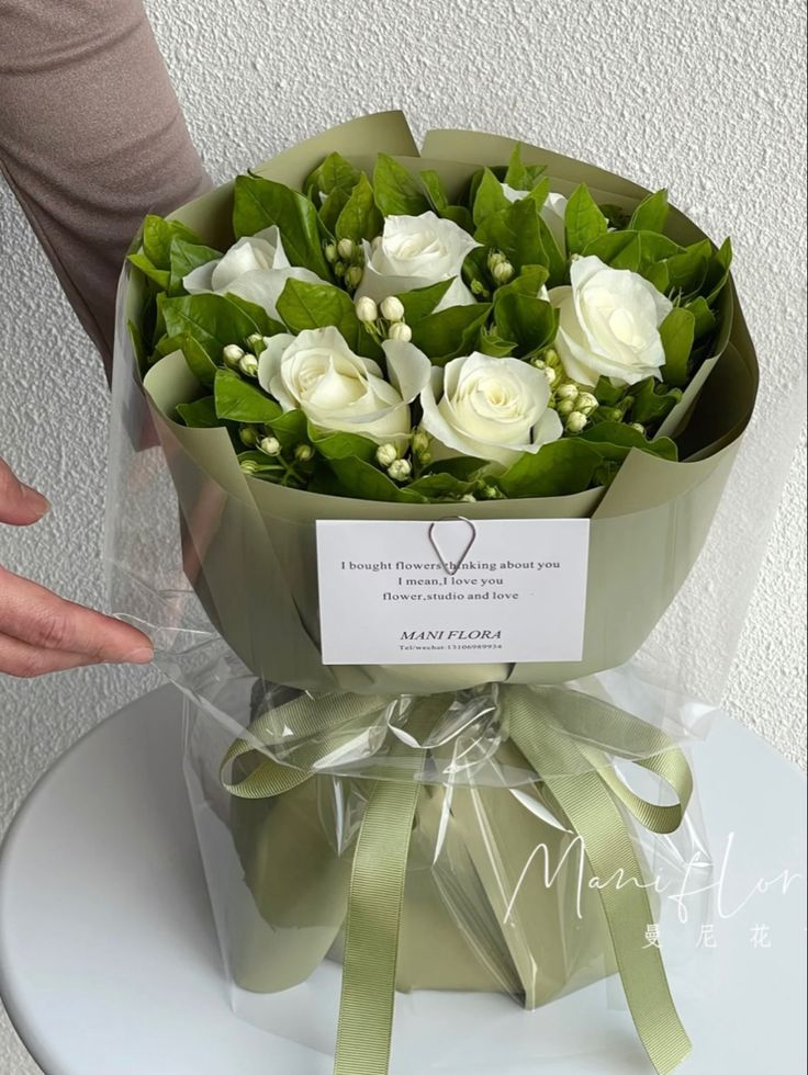 a bouquet of white roses wrapped in cellophane and tied with a green ribbon