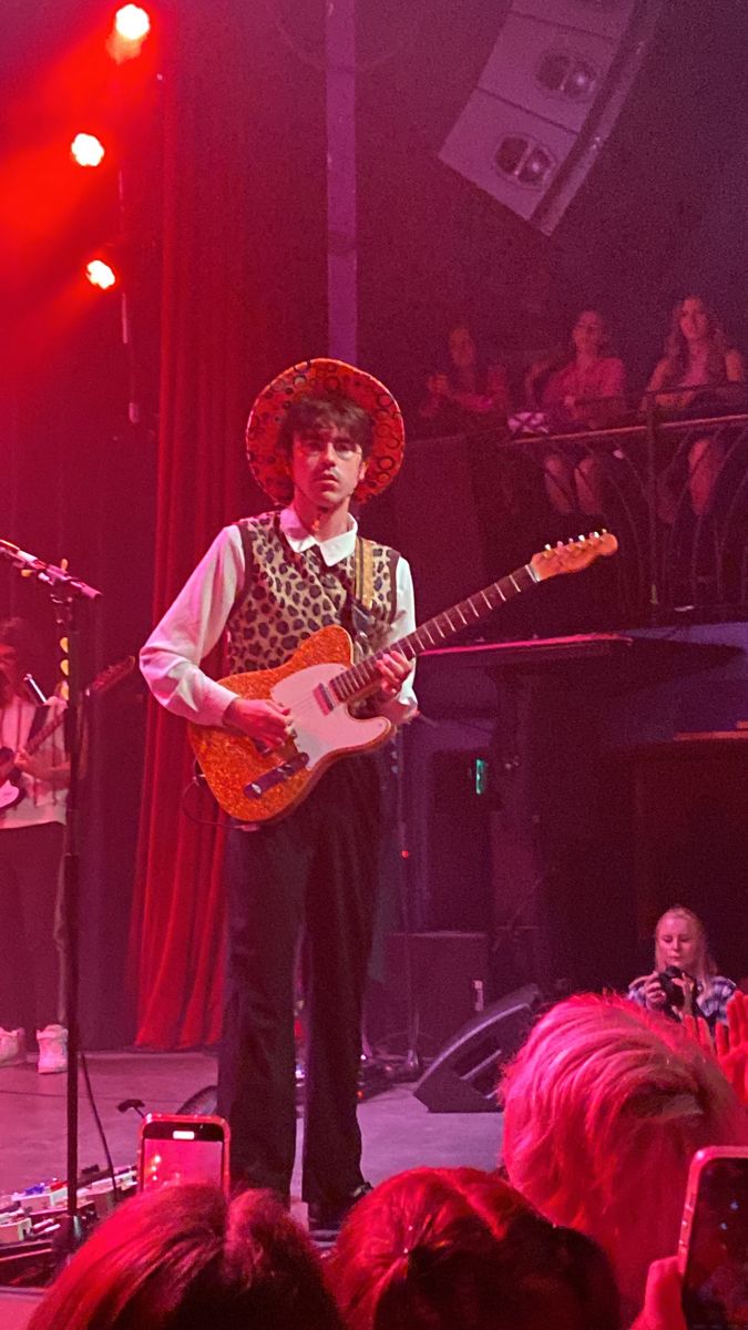 a man in a sombrero playing guitar on stage with other people watching from the audience