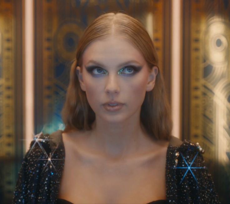 a woman with long hair and blue eyes is looking at the camera while standing in front of a mirror