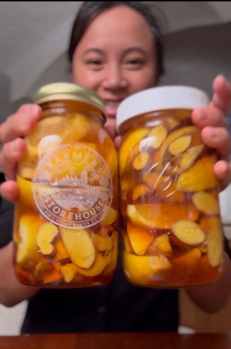 a woman holding two jars filled with pickles