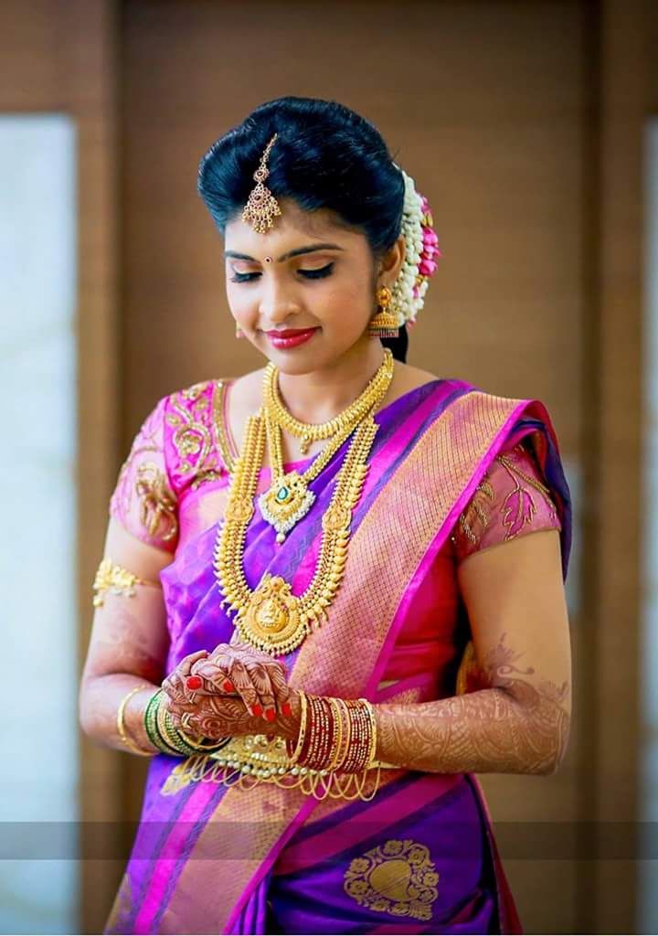 a woman in a purple and pink saree is holding her hands together while wearing gold jewelry